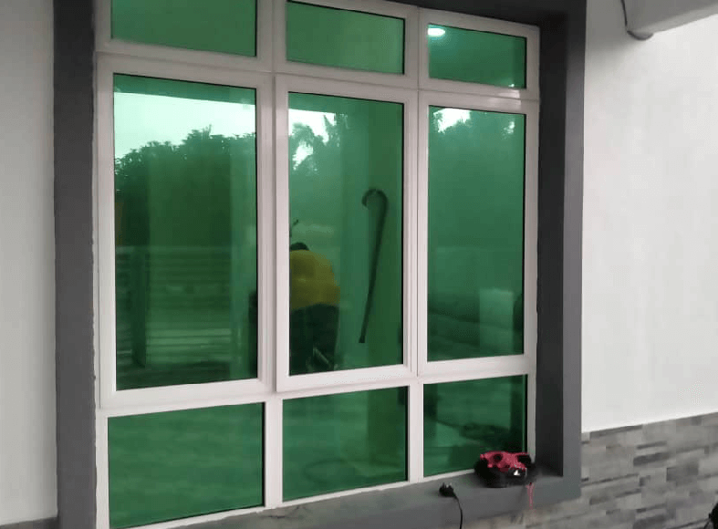 Green-tinted six-pane window with a person in a yellow shirt visible inside and a red cordless tool on the sill outside the frame.