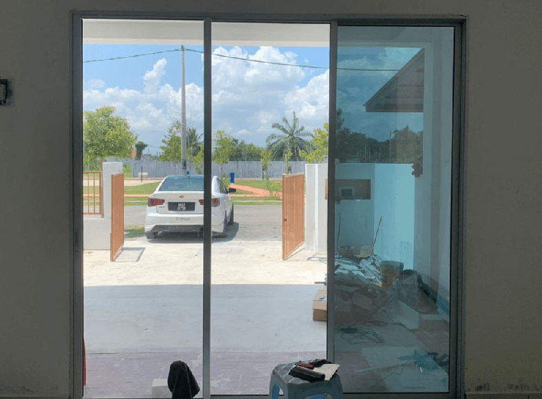 NT1 213 - TINTED HOUSE BUILDING OFFICE WINDOW FILM SHAH ALAM View through a sliding glass door white car parked outside with orange gates open construction debris on the right inside and a blue wall