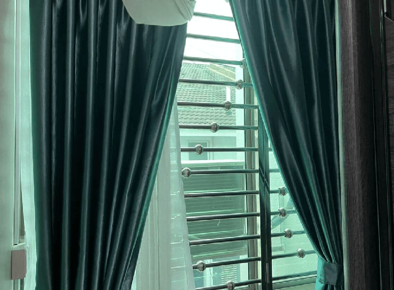 Teal curtains drawn back reveal a window with horizontal metal security bars outside.