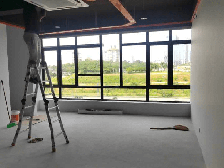 Bright empty room under renovation with a ladder and tools large front windows showing an urban park view